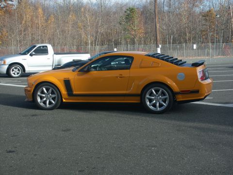 2001 Mercury Grand Marquis - Side view of an orange Ford Mustang GT, parked next to a silver pickup truck.