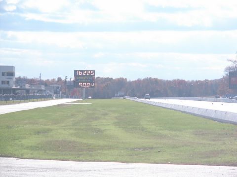 2001 Mercury Grand Marquis - A drag strip scene with a scoreboard displaying times and a distant vehicle on-track vehicle.