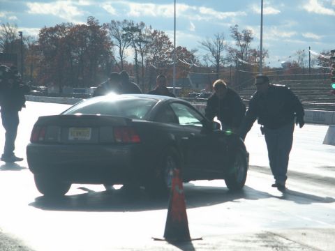 2001 Mercury Grand Marquis - A black coupe is viewed from the rear on a race track with several people around it.