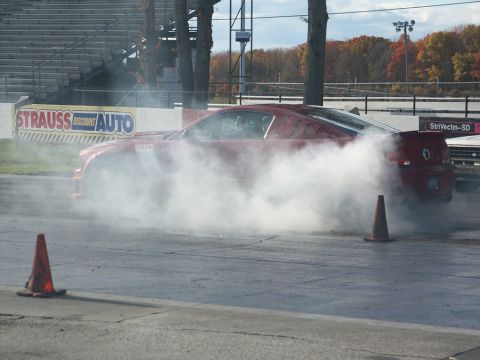 2001 Mercury Grand Marquis - A red sports car performs a burnout on a race track, kicking up a large cloud of smoke.