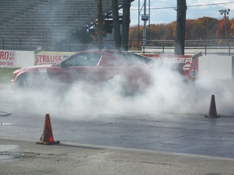 2001 Mercury Grand Marquis - A red sports car performs a burnout on a race track, kicking up a large cloud of smoke.