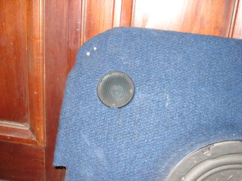 1986 Ford Bronco - A close-up view of a car speaker installed on a blue carpeted panel, with a wooden door in the background.