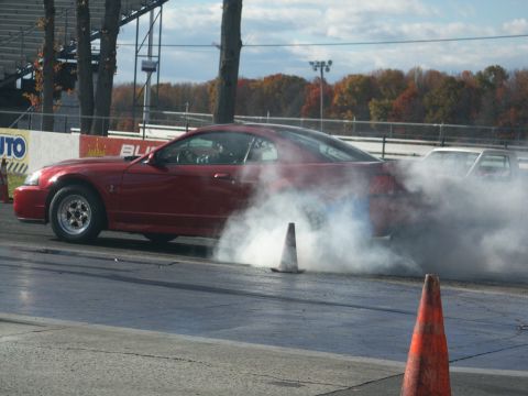 2001 Mercury Grand Marquis - A red coupe performs a burnout on a drag strip, with another vehicle obscured by smoke in the background.