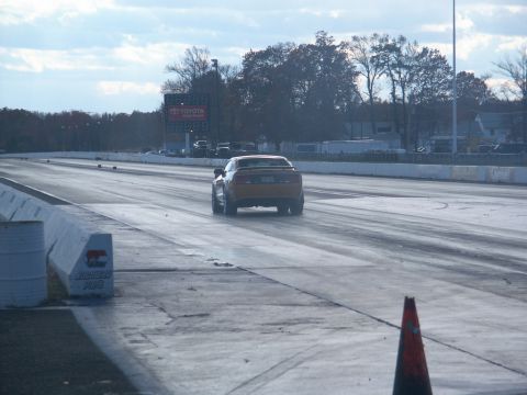 2001 Mercury Grand Marquis - A rear view of an orange muscle car accelerating down a drag strip under a cloudy sky.