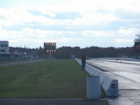 2001 Mercury Grand Marquis - A drag strip scene with a large scoreboard displaying times and a lone car on the track under a cloudy sky.