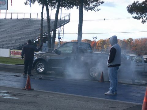 2001 Mercury Grand Marquis - A pickup truck performs a burnout on a drag strip, surrounded by smoke and spectators.