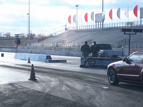2001 Mercury Grand Marquis - A red car is positioned on a drag strip, with grandstands and flags visible in the distance.