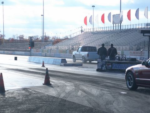 2001 Mercury Grand Marquis - A drag strip scene with a pickup truck and a red car, under a cloudy sky.