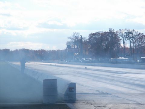 2001 Mercury Grand Marquis - A drag strip scene with a digital scoreboard displaying times, surrounded by trees and a hazy sky.