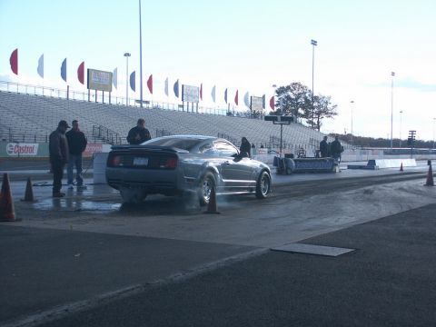 2001 Mercury Grand Marquis - A gray muscle car performs a burnout on the drag strip, with spectators in the background.