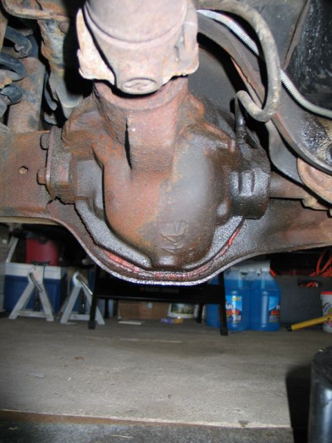 1994 Ford Bronco - Underside view of a vehicle's rear differential housing, showing rust and a connected driveshaft.