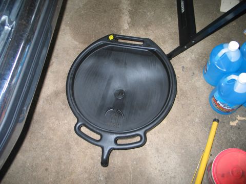 1994 Ford Bronco - A black plastic oil drain pan sits on a concrete floor, with blue fluid containers in the background.