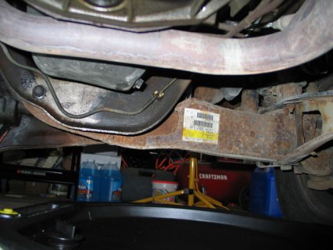 1994 Ford Bronco - Underside view of vehicle frame and exhaust pipe, with a sticker on the rusty metal component.