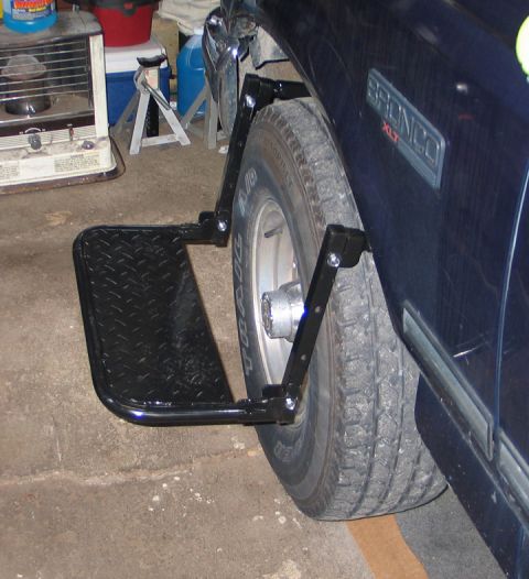 1994 Ford Bronco - A black running board is mounted to the side of a 1994 Ford Bronco, near the front wheel.