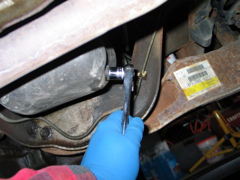 1994 Ford Bronco - Close-up of a hand in a blue glove using a socket wrench on a bolt underneath a vehicle.