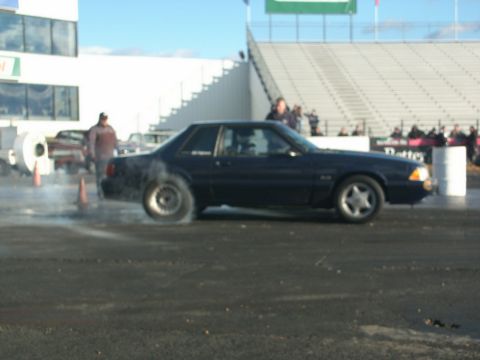 2001 Mercury Grand Marquis - A dark blue coupe is seen performing a burnout on a racetrack, with smoke coming from the rear tire.