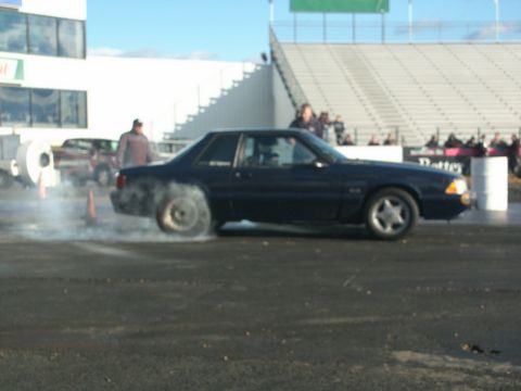 2001 Mercury Grand Marquis - A dark coupe performs a burnout on the drag strip, with a crowd watching from the stands.