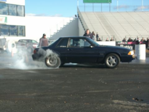 2001 Mercury Grand Marquis - A dark blue coupe performs a burnout at a drag strip event, with a second car visible in the background.