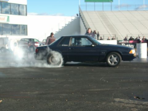 2001 Mercury Grand Marquis - A dark blue coupe is performing a burnout on a drag strip, creating a large cloud of smoke.