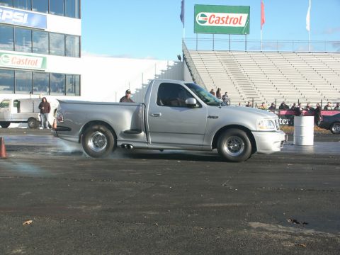 2001 Mercury Grand Marquis - A silver Ford F-150 SVT Lightning performs a burnout at a drag strip event with spectators in the stands.