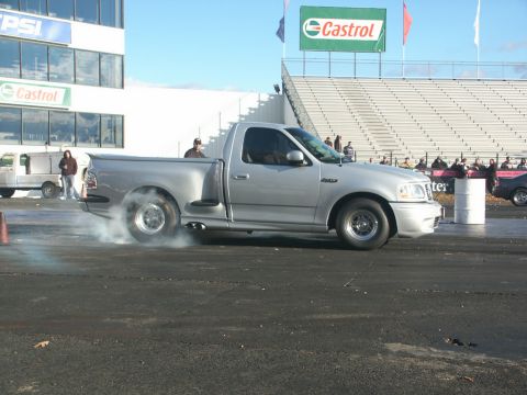 2001 Mercury Grand Marquis - A silver pickup truck performs a burnout on a race track, with spectators in the background.