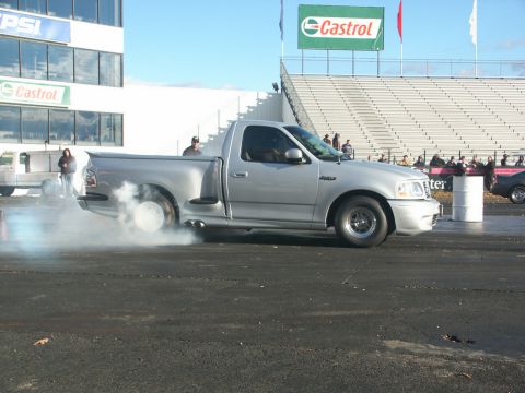 2001 Mercury Grand Marquis - A silver pickup truck performs a burnout on the drag strip, with a crowd watching from the stands.