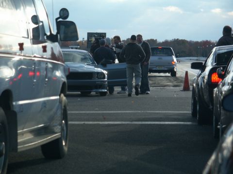 2001 Mercury Grand Marquis - Multiple vehicles and people are gathered on a drag strip under an overcast sky.