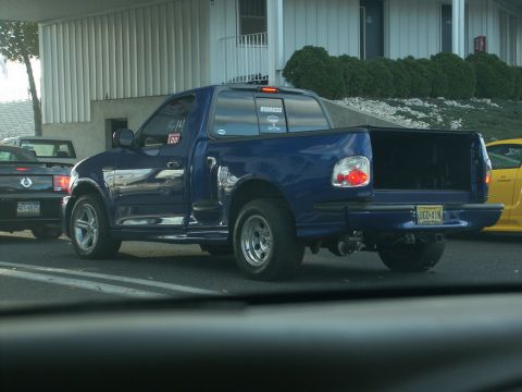 2001 Mercury Grand Marquis - A blue pickup truck is seen from the rear, custom wheels and an open tailgate.