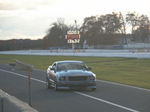 2001 Mercury Grand Marquis - A Ford Mustang is on the track with a digital scoreboard in the background displaying race times.