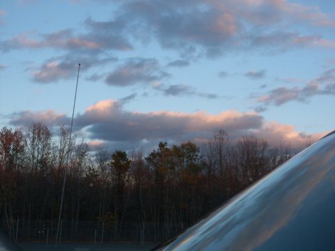 2001 Mercury Grand Marquis - Dusk sky photo taken from beside a vehicle, with the car's whip antenna rising into pink-lit clouds and the sunlit edge of a light-colored…