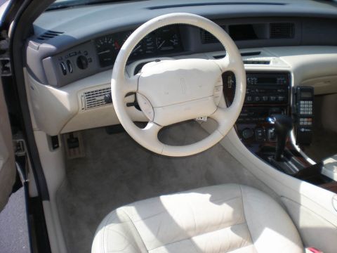 1995 Ford Thunderbird - The interior of a car shows white leather seats, a steering wheel, and a car phone, with a watermark from Supermotors.net.