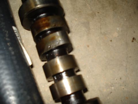 1967 Ford F-250 - A close-up view of a camshaft, showing its lobes and bearing surfaces, with a black hose to the left.