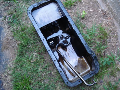 1967 Ford F-250 - A dirty oil pan with its internal pickup tube is shown resting on the ground.