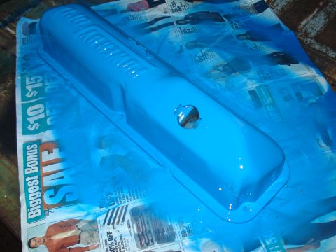 1967 Ford F-250 - A blue valve cover is being spray painted while resting on newspaper advertisements.