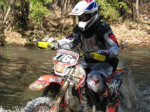 1990 Ford Bronco - close-up of a rider on muddy dirt bike number 276 wading through a creek in worn off-road gear.