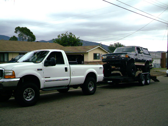 White Ford F-250 towing a black Ford Bronco on a trailer, side view