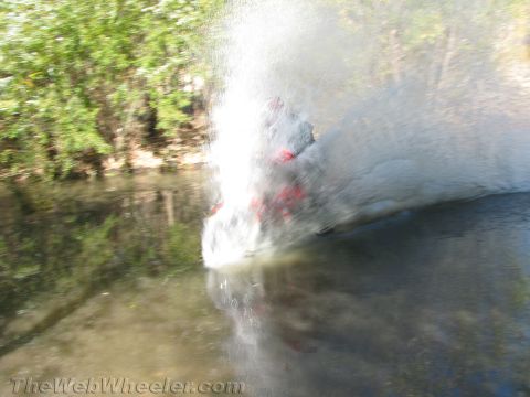 1990 Ford Bronco - motion-blurred burst of water spray with a glimpse of a red vehicle as a rider crashes through a creek.