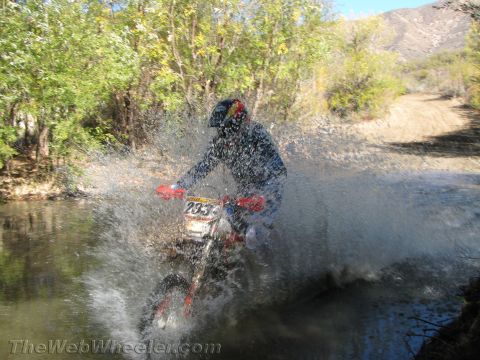 1990 Ford Bronco - rider on dirt bike number 235 blasts through a creek, throwing up a heavy fan of water spray on a canyon trail.