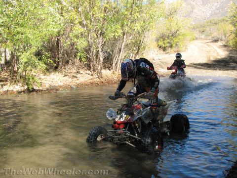 1990 Ford Bronco - rider guides a sport quad ATV across a river crossing as a second quad follows through the spray behind on the dirt trail.