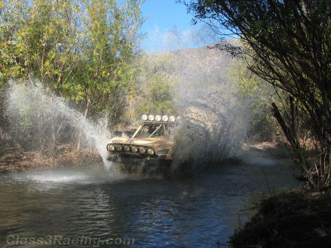 1990 Ford Bronco - off-road race truck with a roof light bar hits a river crossing head-on, exploding water into a massive wall of spray.