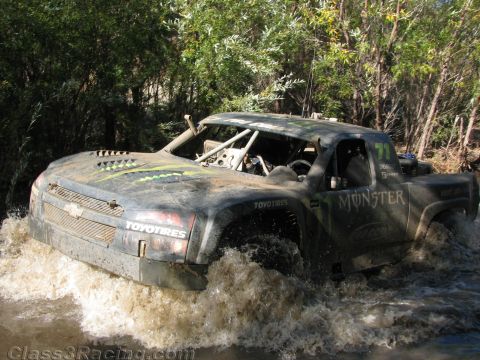 1990 Ford Bronco - Chevrolet-grilled off-road race truck, number 71 with Monster and Toyo Tires decals, churns through a muddy river crossing.