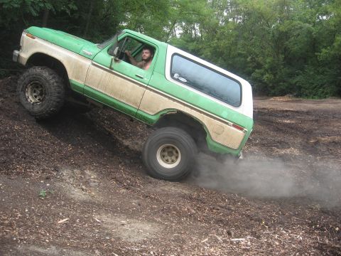 1979 Ford Bronco - A man drives a lifted green and white Ford Bronco up a steep, loose dirt incline, creating a cloud of dust.