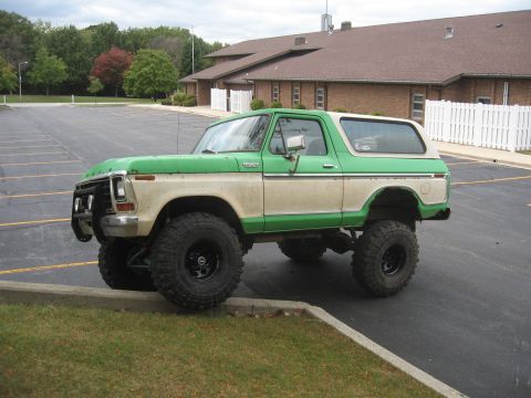 1979 Ford Bronco - This lifted SUV is parked with its front-left tire on a curb, showing its off-road modifications.