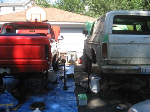 1979 Ford Bronco - Two trucks, a 1979 Ford Bronco and a red pickup, are undergoing maintenance outdoors.
