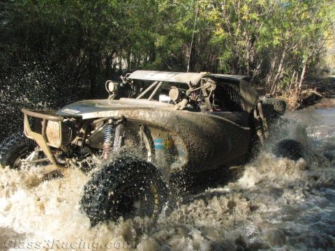 1990 Ford Bronco - mud-soaked off-road buggy with large knobby tires plows through a stream, throwing water in all directions.