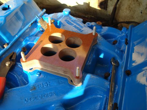 1967 Ford F-250 - Close-up of a blue engine intake manifold with a carburetor gasket and a wrench, suggesting engine work.