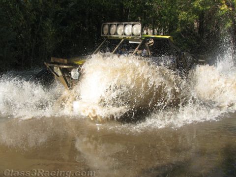 1990 Ford Bronco - off-road buggy with a roof light bar throws a tall fan of brown water while crossing a river.