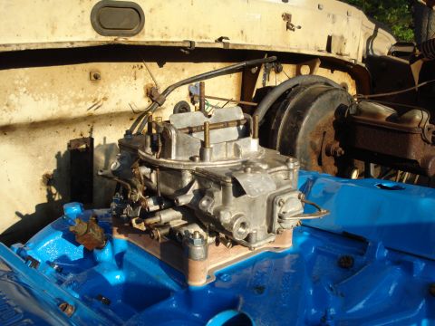 1967 Ford F-250 - Close-up of a carburetor mounted on a freshly painted blue engine block, with engine bay components visible in the background.