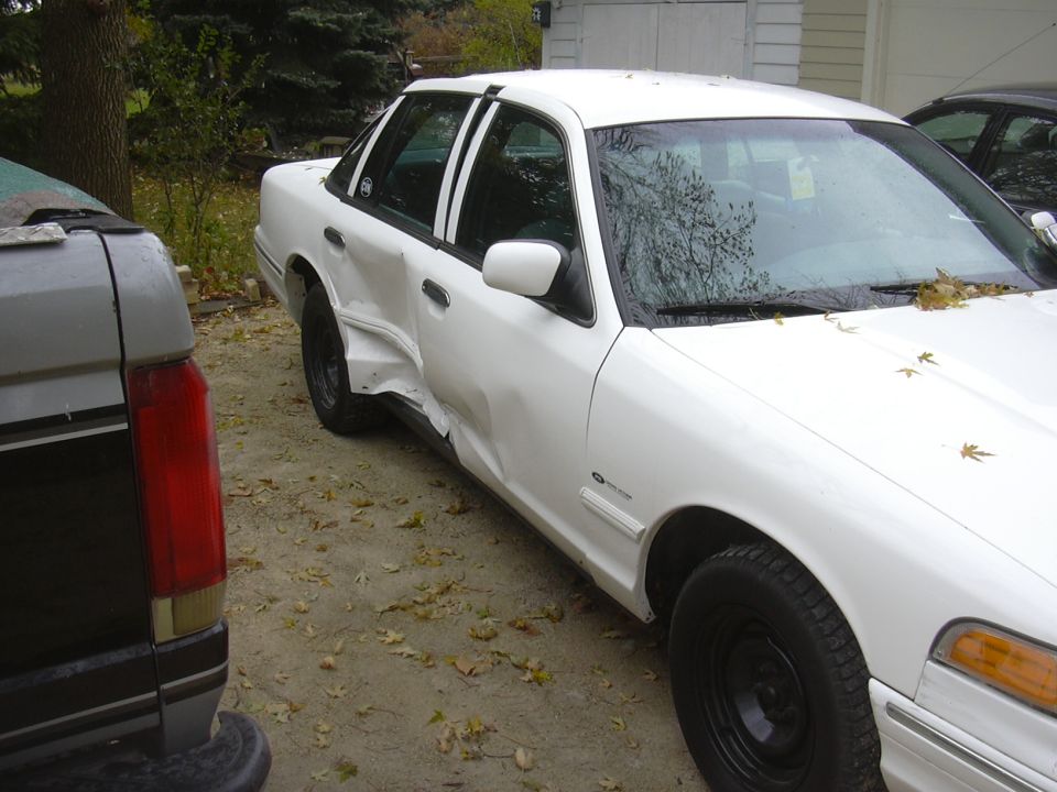 White sedan with severe side damage, parked next to a dark pickup truck