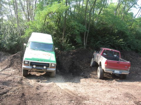 1979 Ford Bronco - Two trucks are parked on a dirt path surrounded by trees.